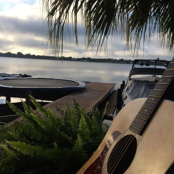 An acoustic guitar on the dock at sunrise, the trampoline and boat beyond